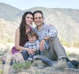Miles Lessen, his wife and son sitting on the ground outside with mountains behind them