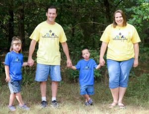 Regina Bradley standing outside with her husband and two young children. She and her husband are both wearing yellow t-shirts while the two children are wearing blue t-shirts. 