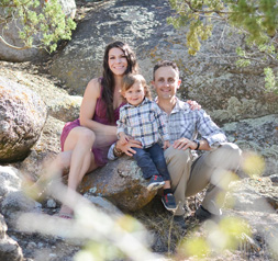 Miles Lessen with wife and young son posing together outside on rocks