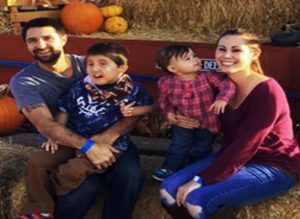 Lauren Hughes, sitting with her husband and two young sons, outside, with pumpkins and hay surrounding them. 