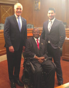 Edward Mitchell, sitting in his powerchair, next to Senator Bob Casey and Former ABLE NRC Director, Chris Rodriguez. They are all in a Senate Office Building room. 