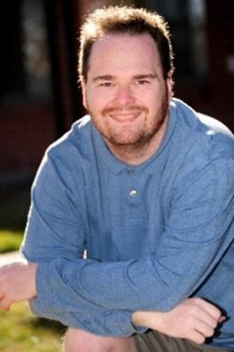 Ty Erd Smith, a white man with light, brown hair and a short beard posing an smiling for the camera.