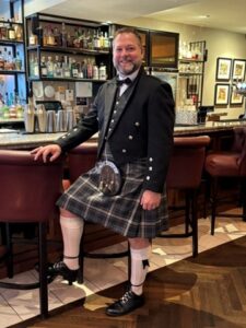 Kevin McClelland posing while wearing a kilt next to a bar